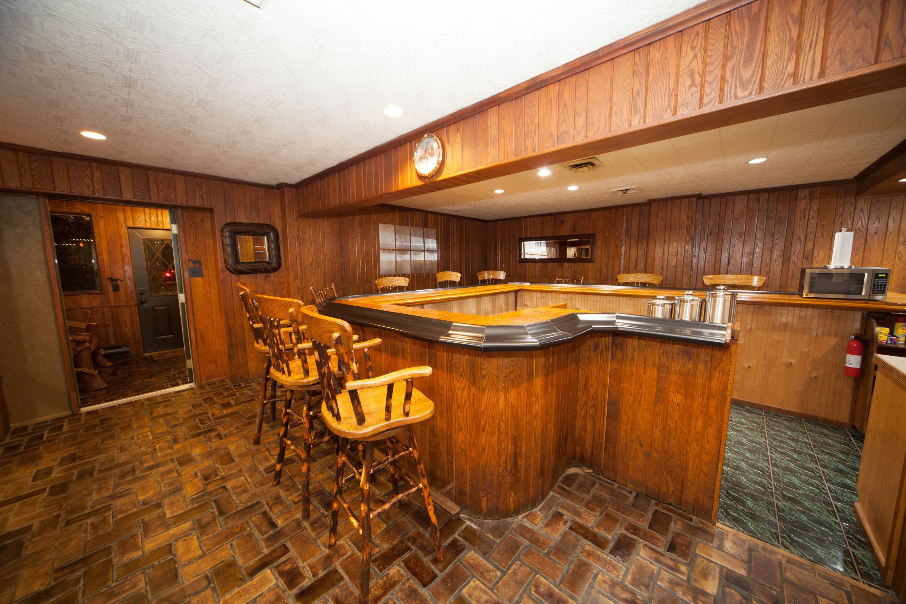 Una zona de bar con paneles de madera, un reloj y un microondas.