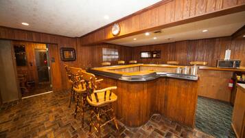 A bar area with wooden paneling, a clock, and a microwave.