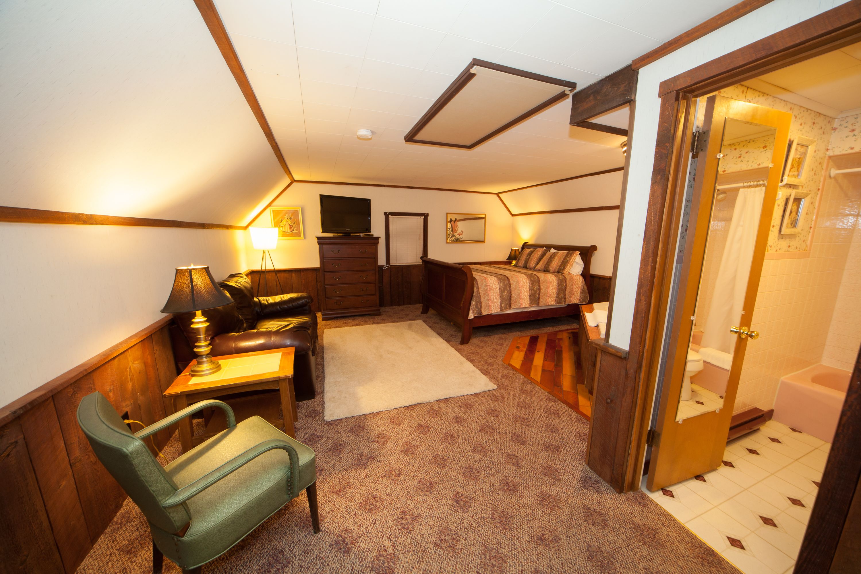 A compact room with a bed, a desk with a lamp, a chair, and a television.