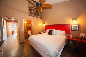 Una habitación de hotel con una cama grande, cabecera roja, ventilador de techo y un escritorio con silla.