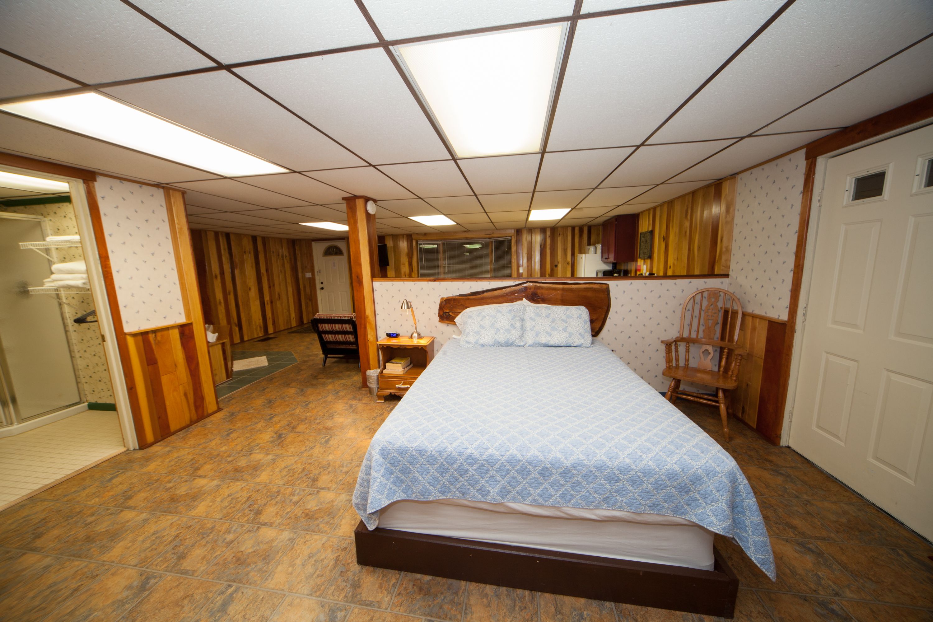 Un dormitorio con una cama grande, paredes de madera, una silla de madera y una mesita.