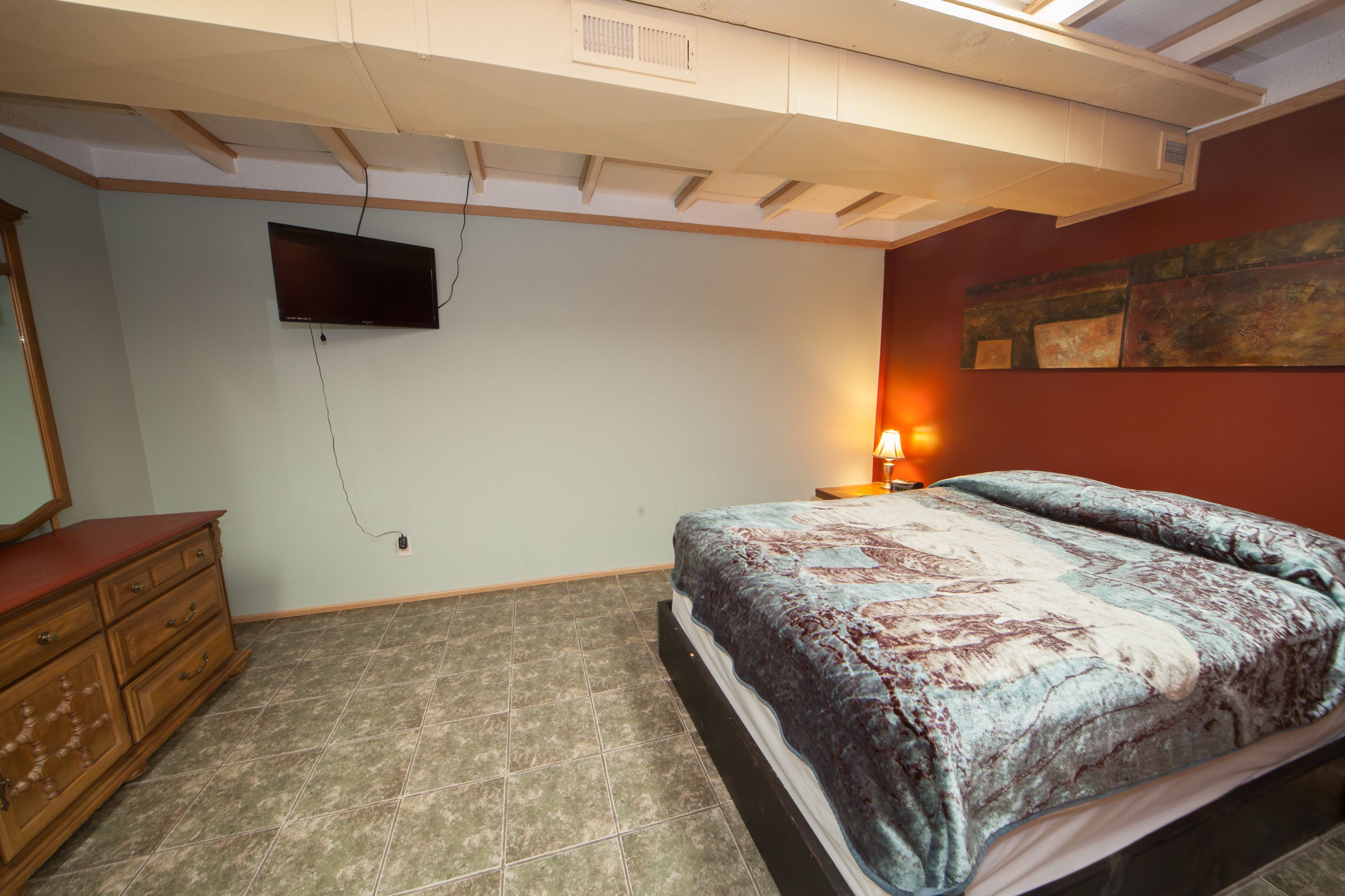 Une chambre à coucher comprenant un lit, une commode, un téléviseur à écran plat fixé au mur et un tableau accroché au mur.