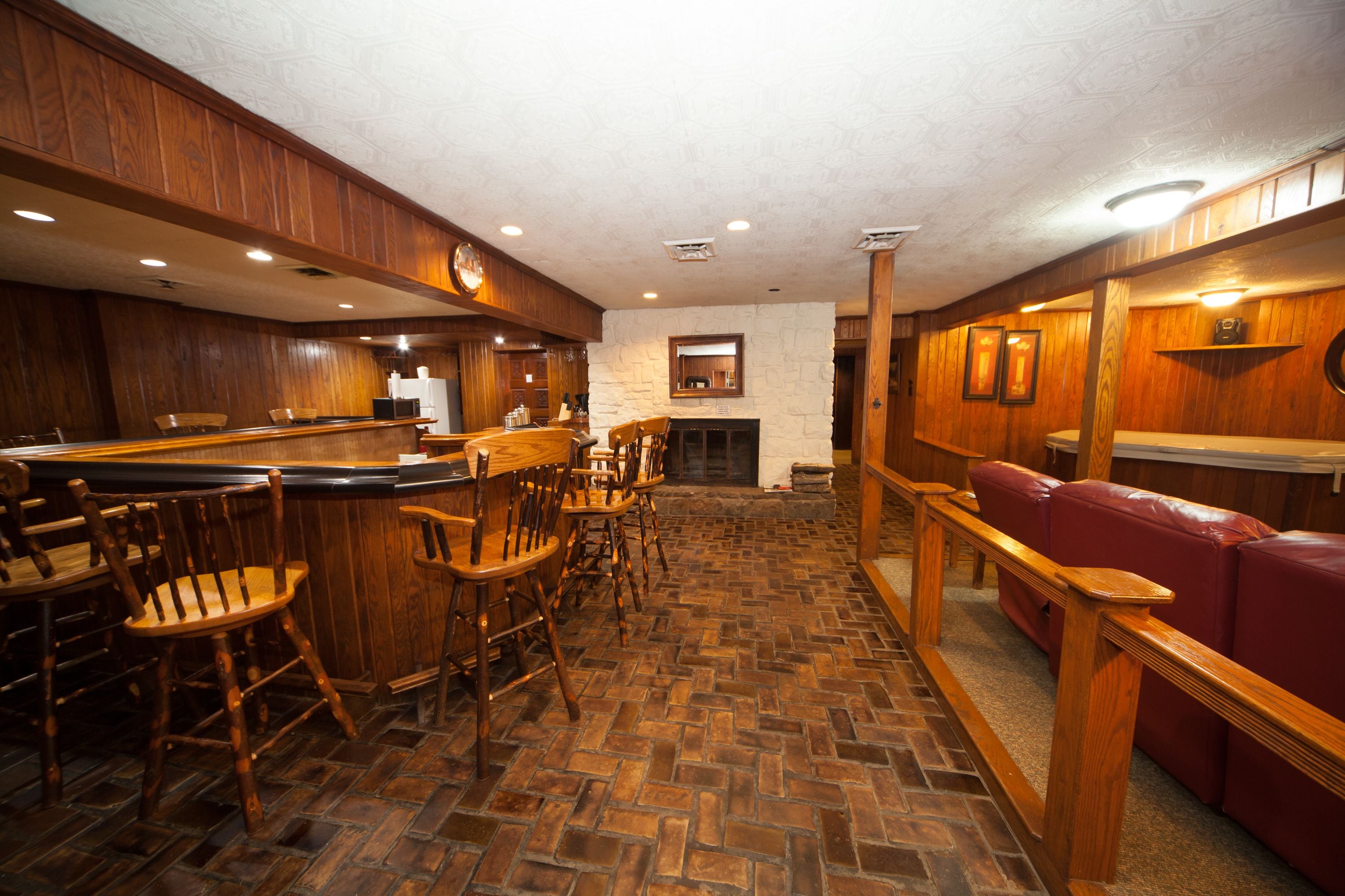 Zona de bar con mobiliario de madera, chimenea de piedra y sofá de cuero rojo.