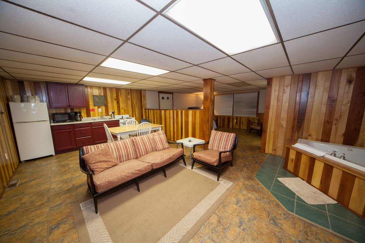 A compact kitchen with a refrigerator, microwave, and coffee maker. There is a dining table with chairs and a sofa with striped cushions. A small white table and a chair are also visible.