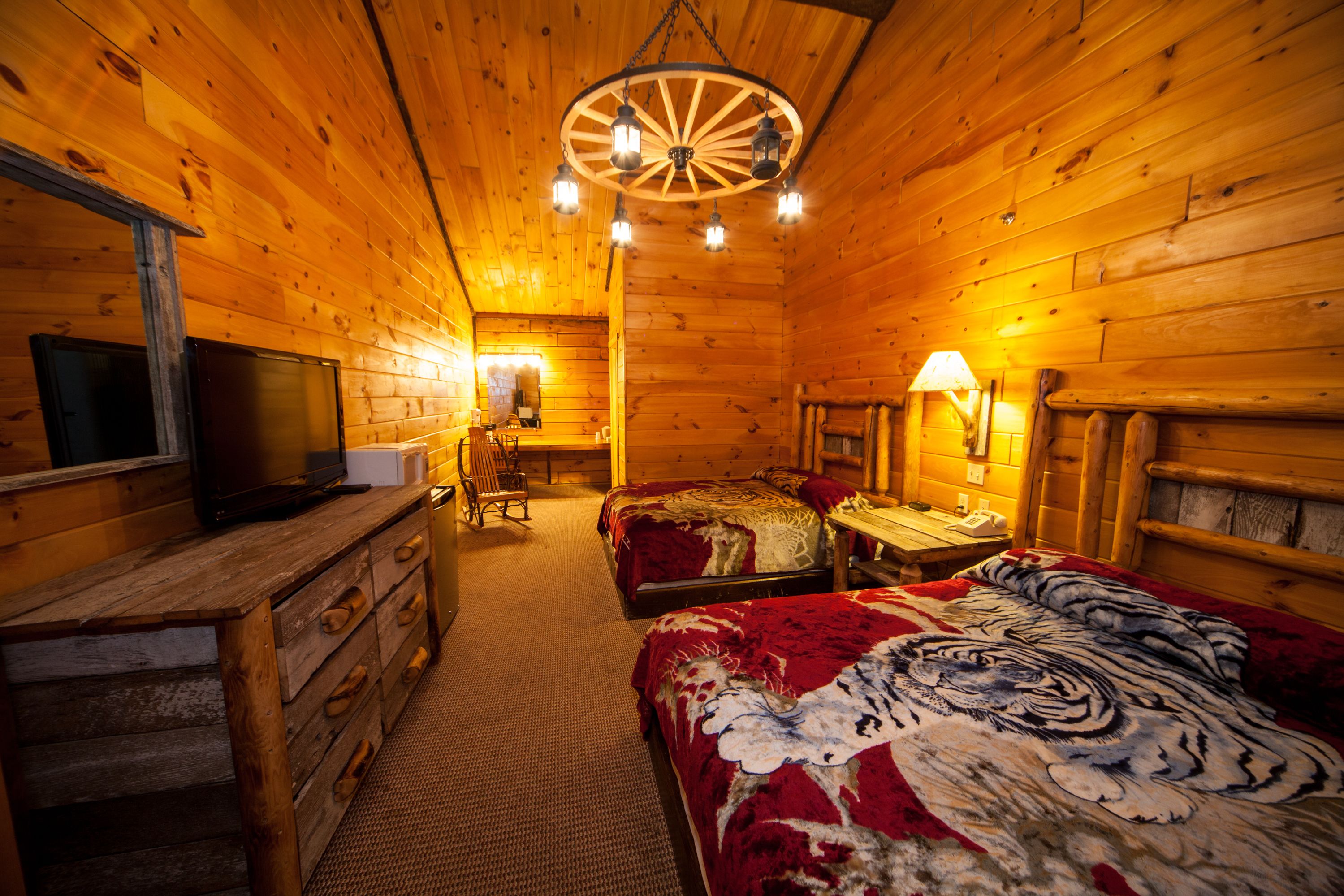 Una stanza in baita di legno con soffitto in legno, un letto con coperta a motivi di tigre, una scrivania con lampada e un televisore su un comò.