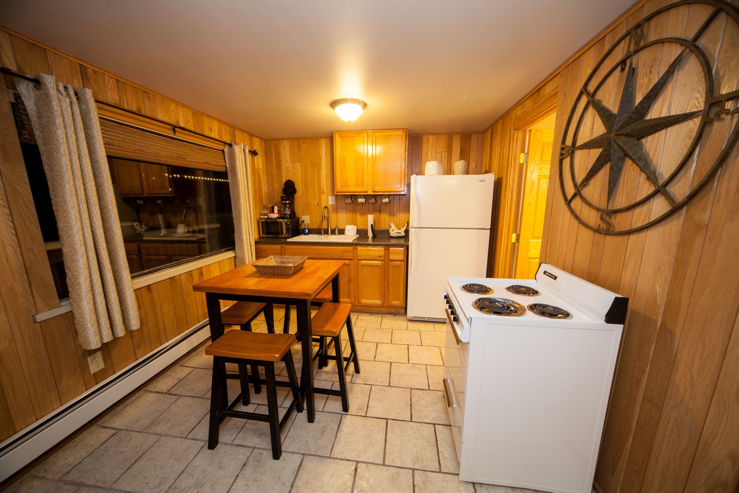 Una cocina compacta con armarios de madera, un refrigerador blanco, una estufa y una mesa con bancos.