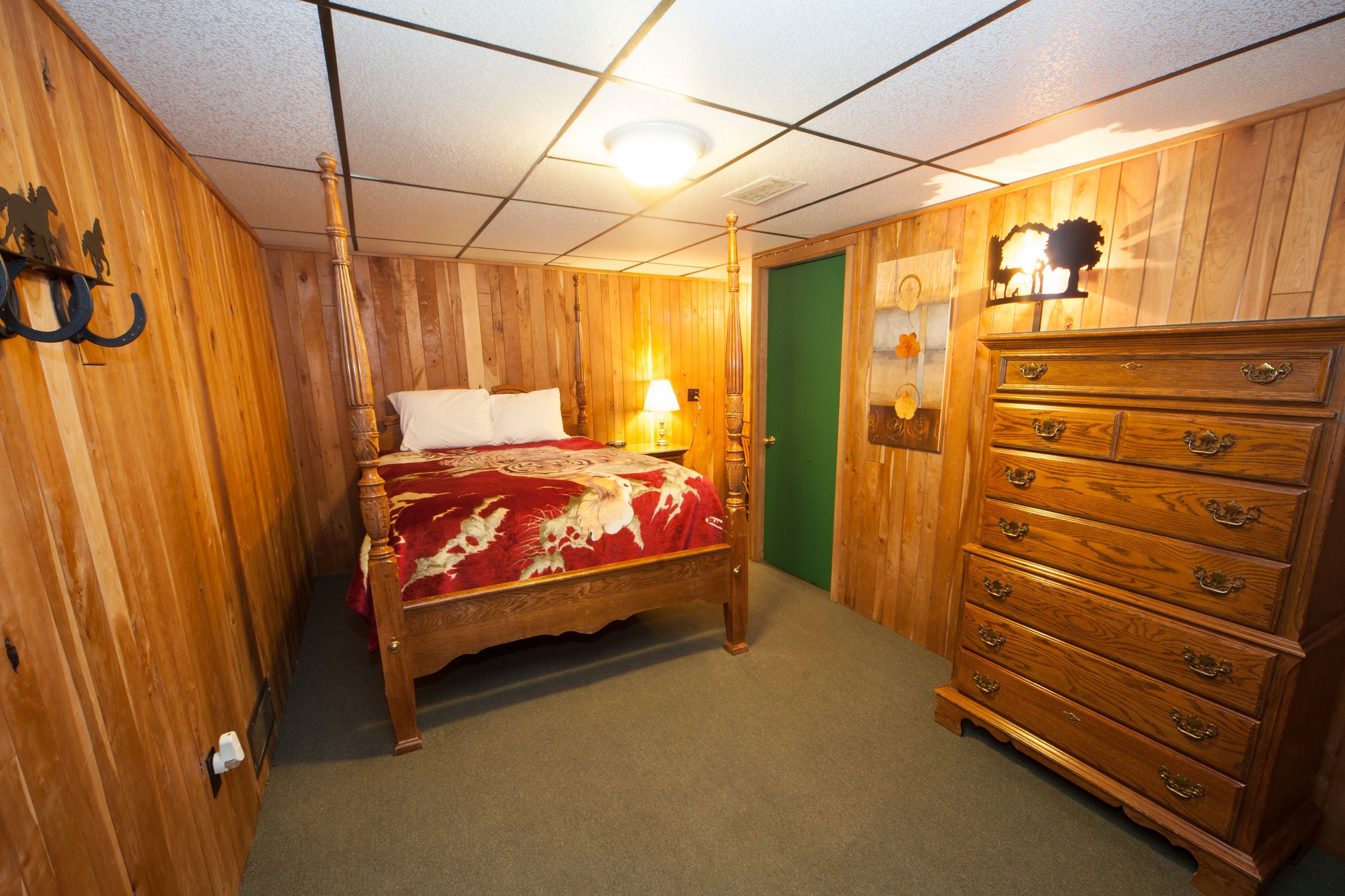 A wooden room with a bed, dresser, and a green door.