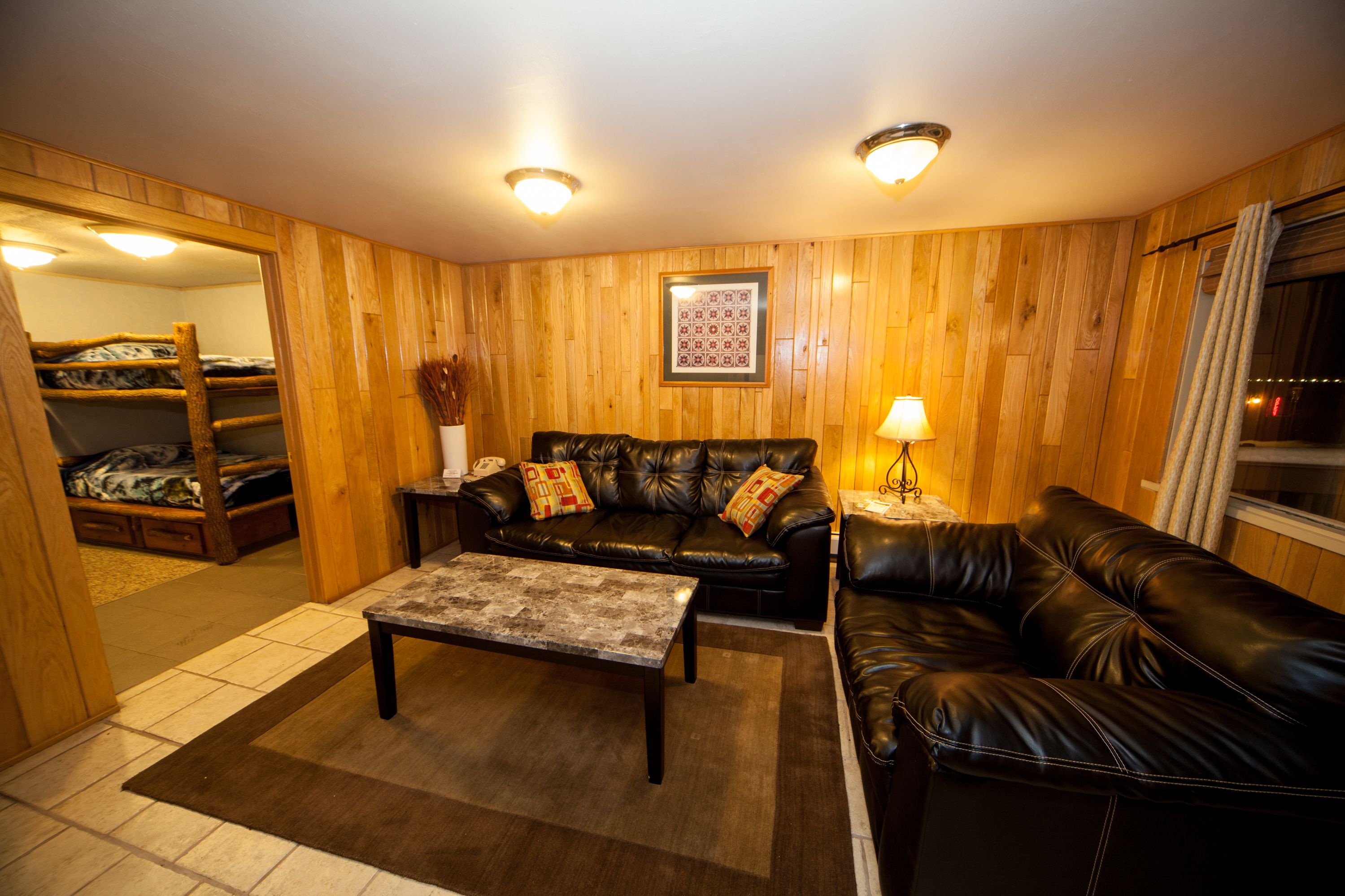 A cozy room with a leather sofa, a small coffee table, and a wooden bunk bed in the background.