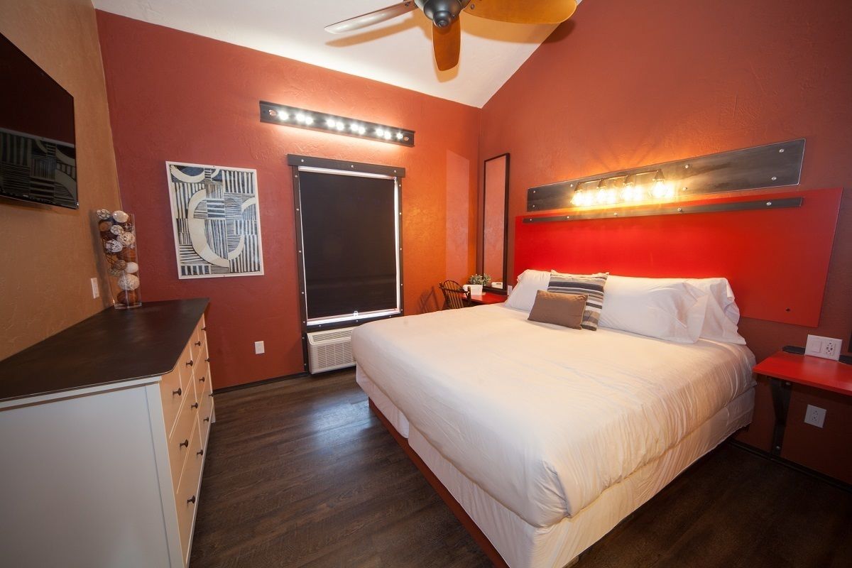 Une chambre avec un grand lit, un ventilateur de plafond, une fenêtre avec des stores et une commode.
