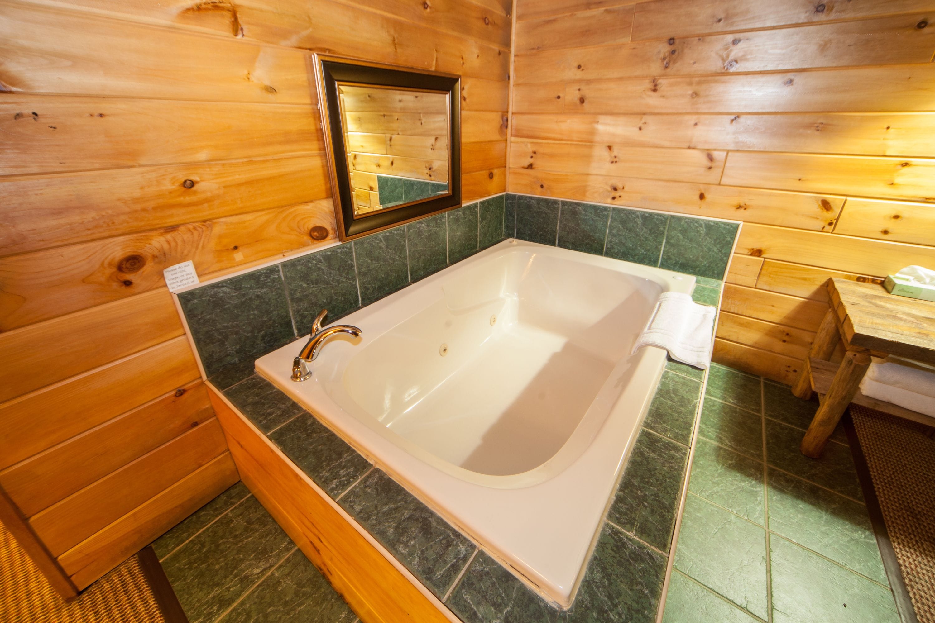 Un baño de cabaña de madera con una bañera grande, paredes de azulejos verdes y un tocador de madera.