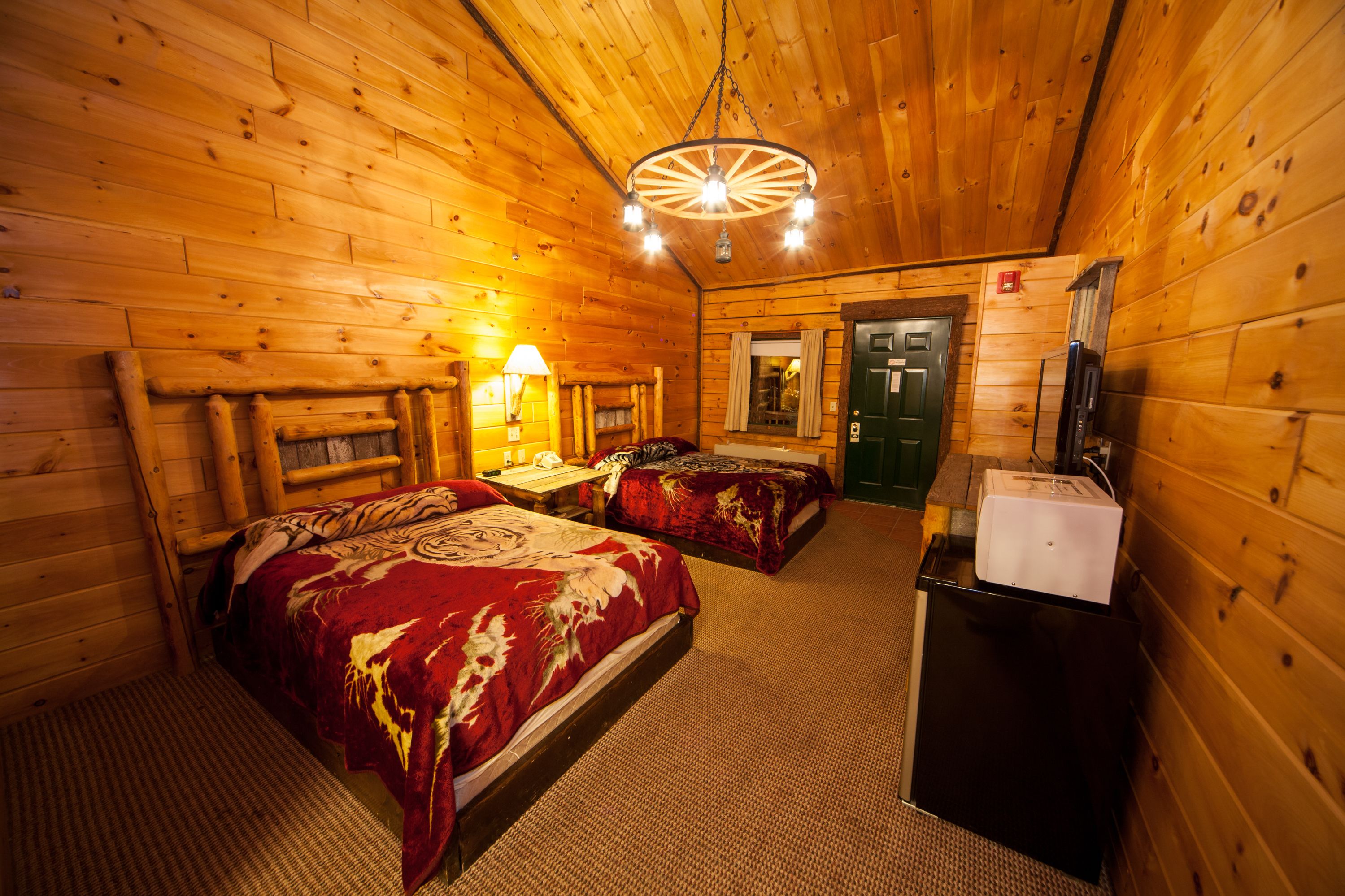 A log cabin room with two beds, a desk, a lamp, and a refrigerator.