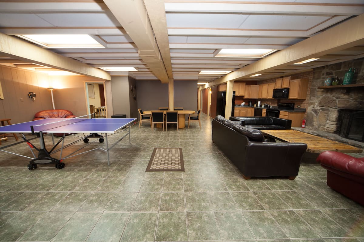 A spacious living area with a ping pong table, a sofa, a fireplace, and a kitchen in the background.