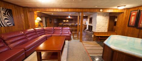 A spacious living room with a large leather sectional sofa, a wooden coffee table, and a hot tub.