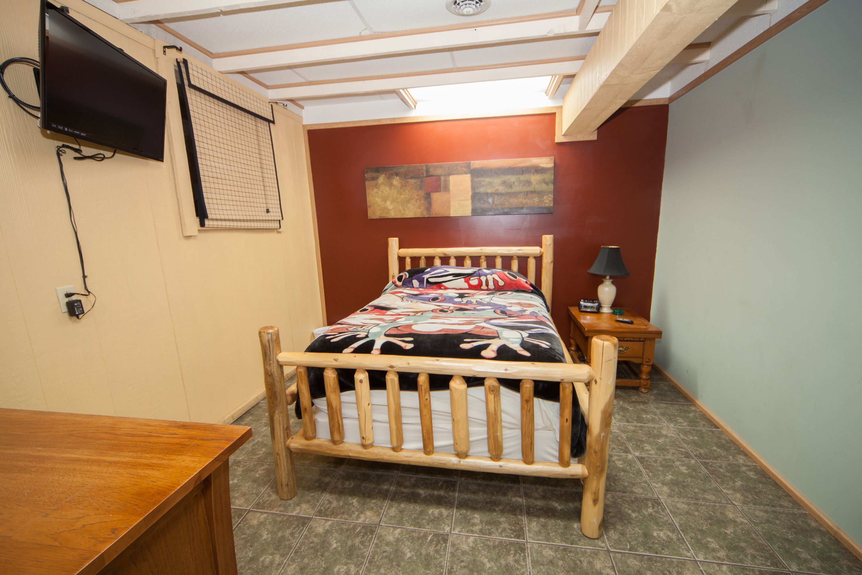 Una camera da letto con un letto di legno, un comodino, una lampada e una TV a muro.