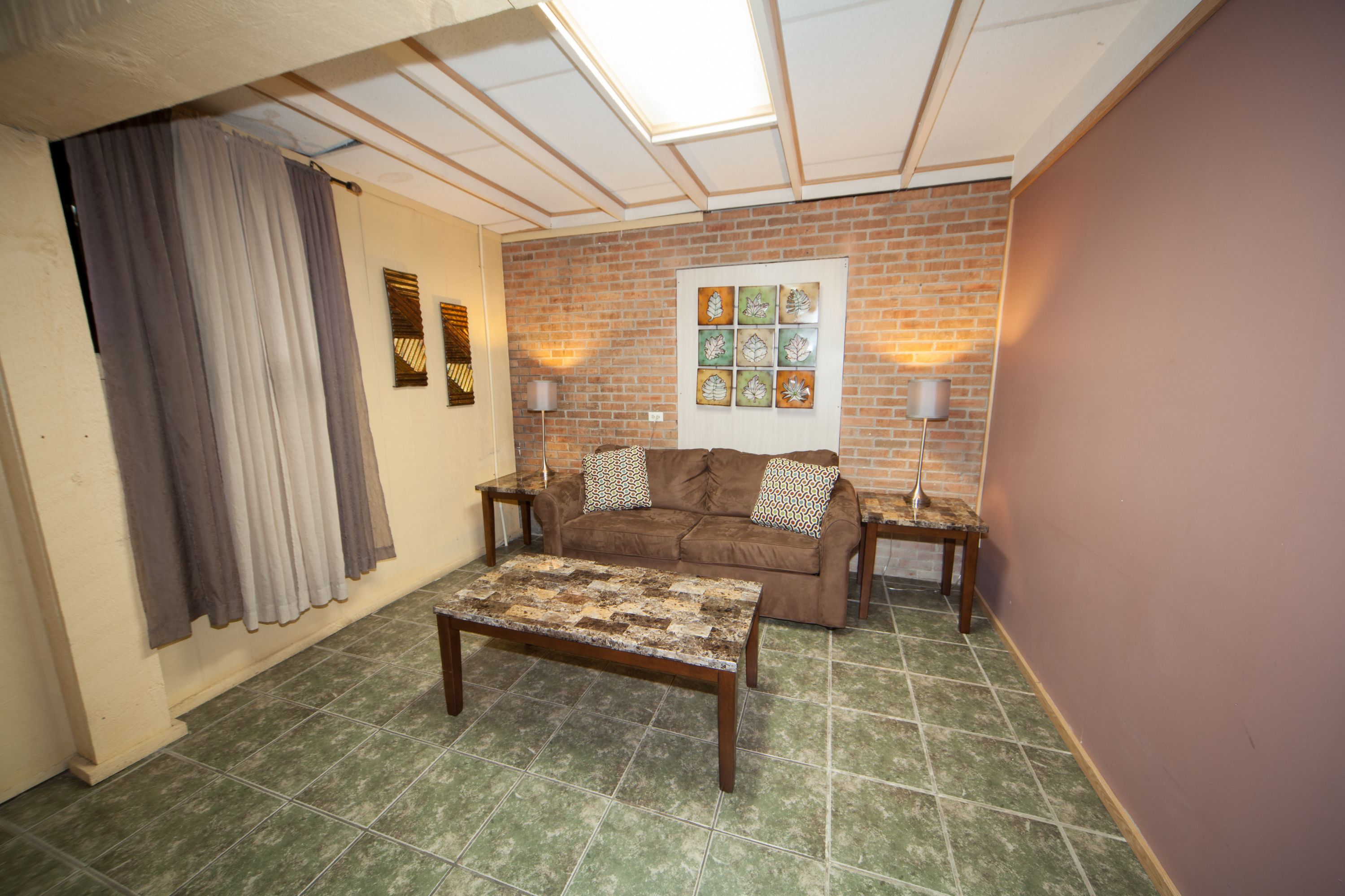 A living room with a brown sofa, a patterned coffee table, and a brick wall.