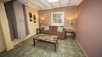 A living room with a brown sofa, a patterned coffee table, and a brick wall.