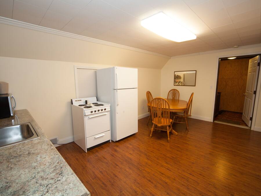 A compact kitchen with a stove, refrigerator, and sink. There is a dining table with chairs and a wooden door leading to another room.