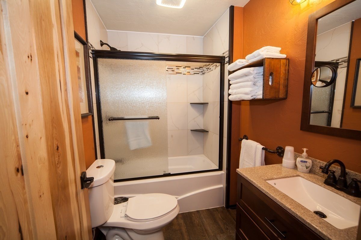 A bathroom with a glass-enclosed shower, a white toilet, a sink with a mirror, and a wooden cabinet with towels.