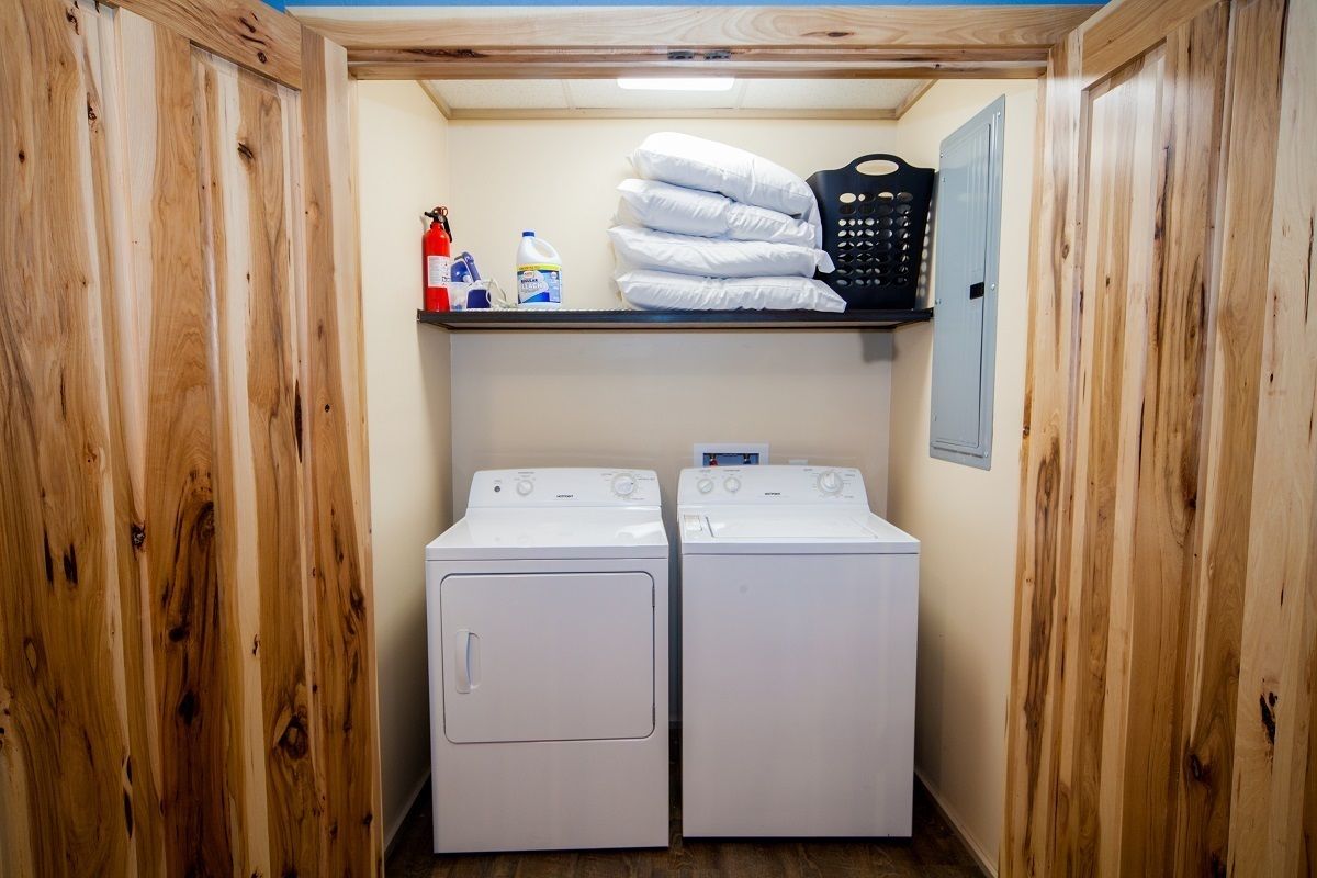 A laundry room with two white washing machines, a shelf with towels and cleaning supplies, and a fire extinguisher.