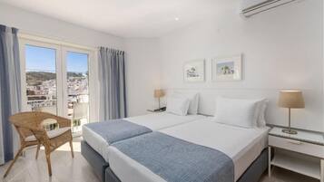 Ein Hotelzimmer mit einem großen Bett, einem Sessel, einem Nachttisch und Blick auf die Stadt durch das Fenster.