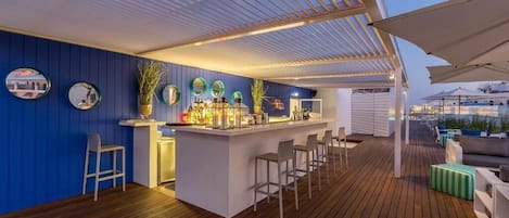 Zona de bar con suelo de madera, una barra blanca y taburetes.