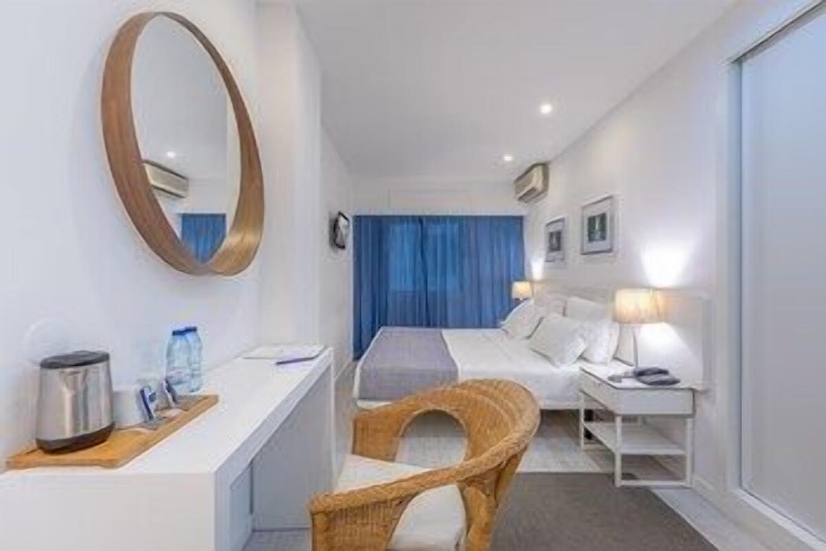 Habitació d'hotel amb llit, taula de nit, làmpada, cadira i un mirall gran.