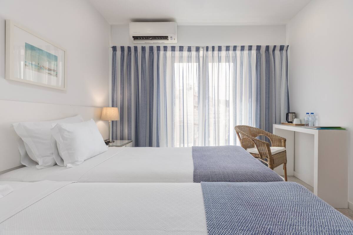 Ett hotellrum med en säng, ett skrivbord, en stol och ett fönster med gardiner.