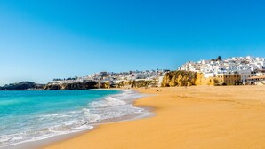 Une plage bordée de bâtiments blancs, avec une eau d’un bleu limpide et un rivage sablonneux.