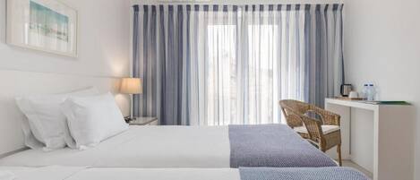 A hotel room with a bed, a desk, a chair, and a window with curtains.