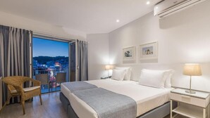 Une chambre d’hôtel avec un lit, une chaise, une table de chevet et une vue sur la ville au crépuscule.