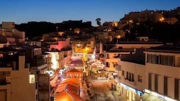A nighttime view of a city street with buildings, shops, and a hill in the background.