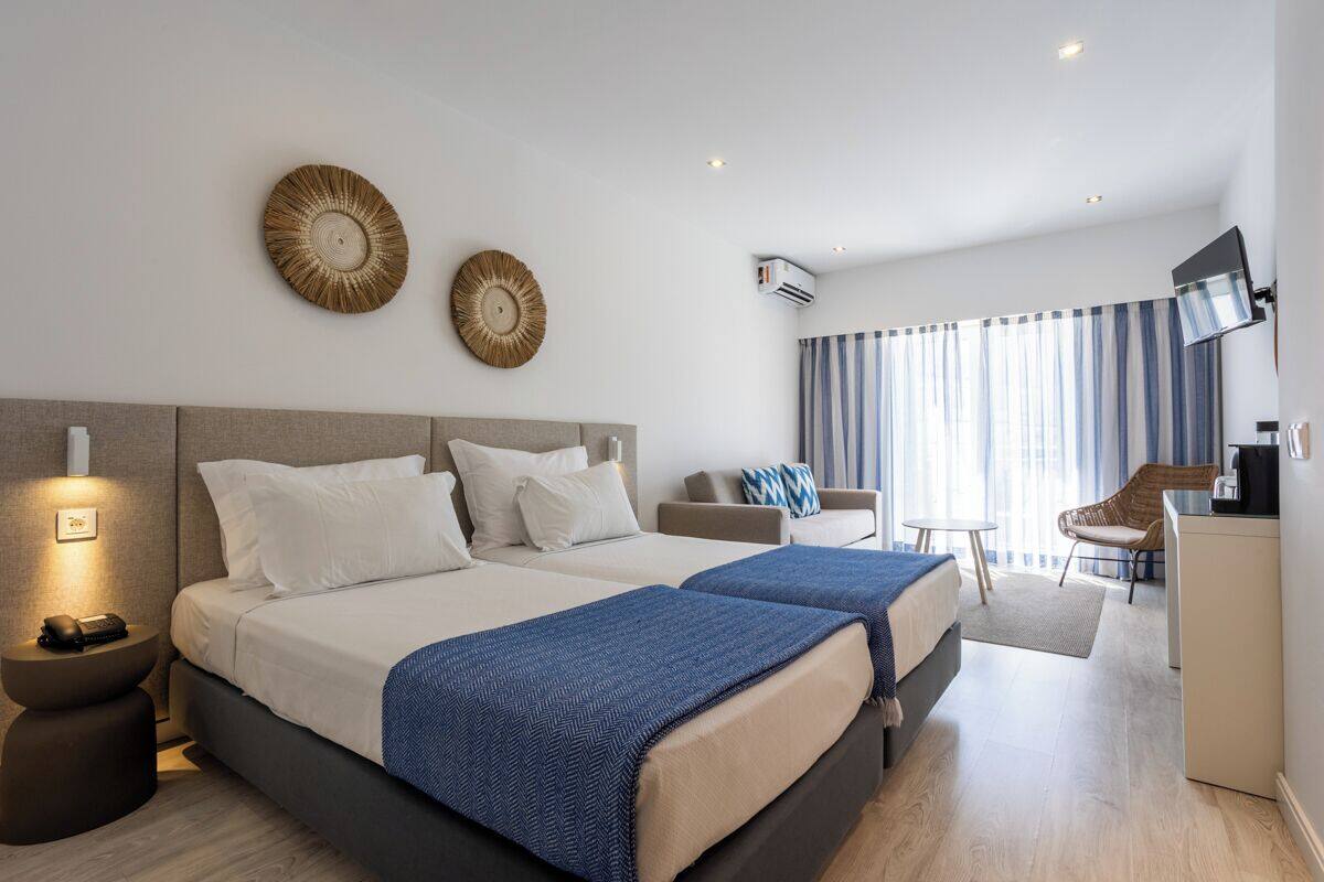 Ett hotellrum med två sängar, ett skrivbord, en stol, en TV och ett fönster med gardiner.
