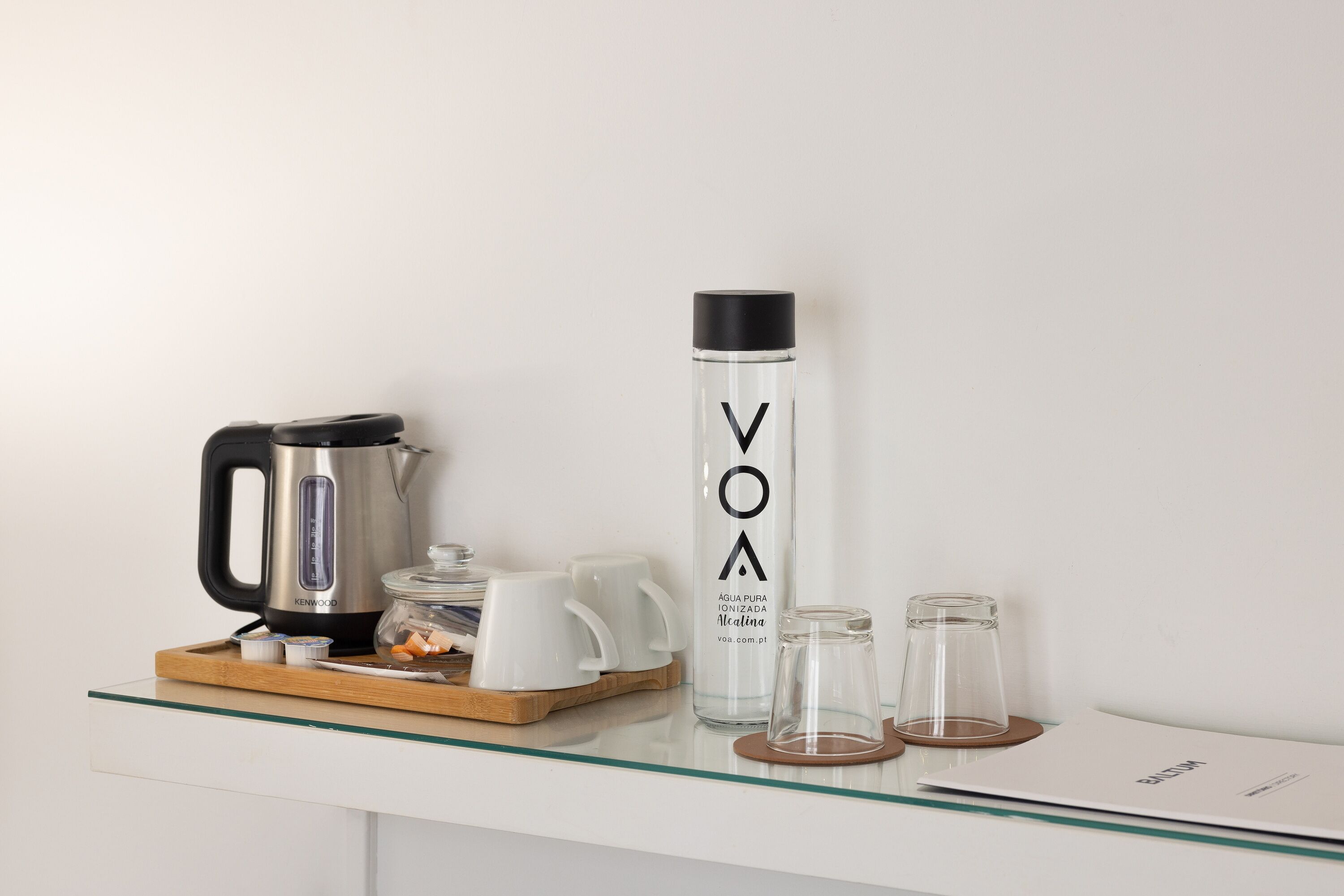 A kitchen counter with a kettle, a water bottle, and two glasses on a tray.