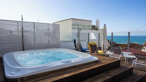 Une terrasse sur le toit équipée d’un jacuzzi, de chaises longues et d’une balustrade en verre donnant sur la mer.
