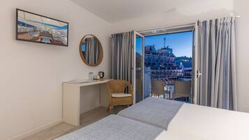 Et hotelværelse med seng, skrivebord, stol, stort vindue og balkon.