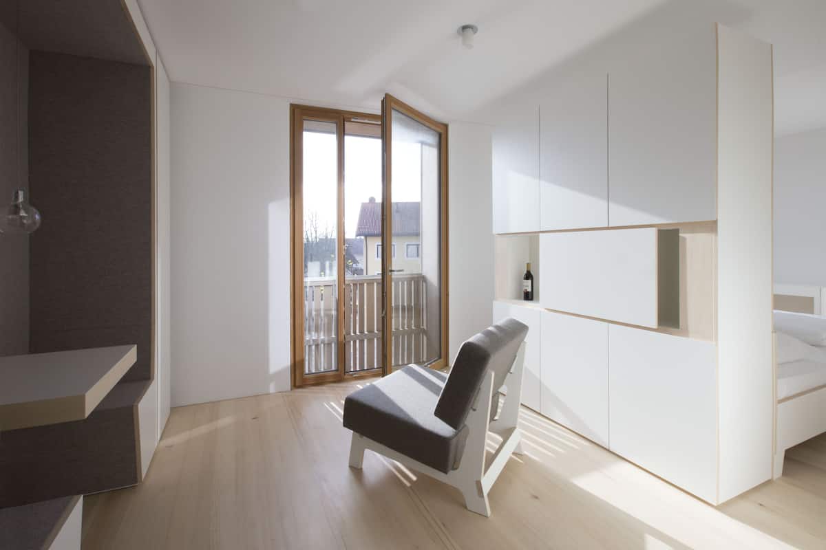 Une pièce moderne et minimaliste, dotée d’une banquette intégrée, d’une petite table et d’une porte-fenêtre coulissante donnant sur un balcon.