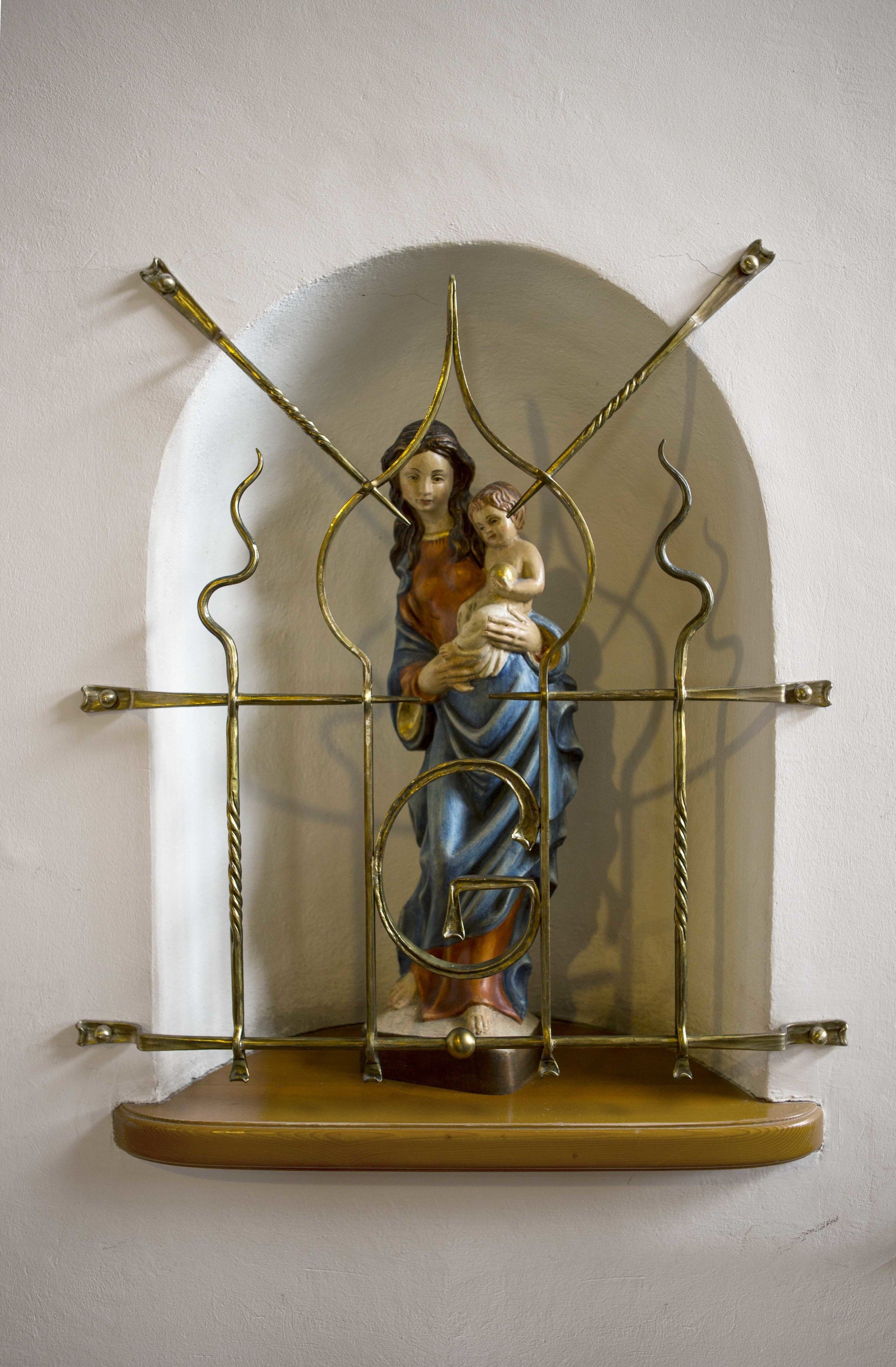 A religious statue on a metal stand with a white wall background.