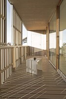 Una terraza de madera con una mesa y sillas blancas, ventanas amplias y vistas al cielo.