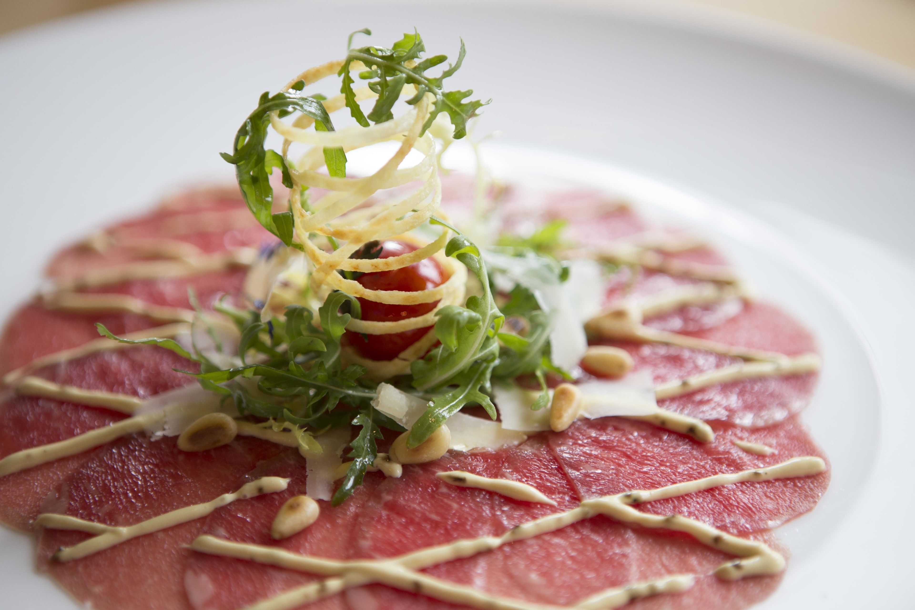A plate of raw meat with a garnish of greens and nuts, drizzled with a sauce.