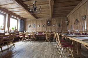 Un comedor con paneles de madera, mesas y sillas de madera, una araña y relojes en la pared.