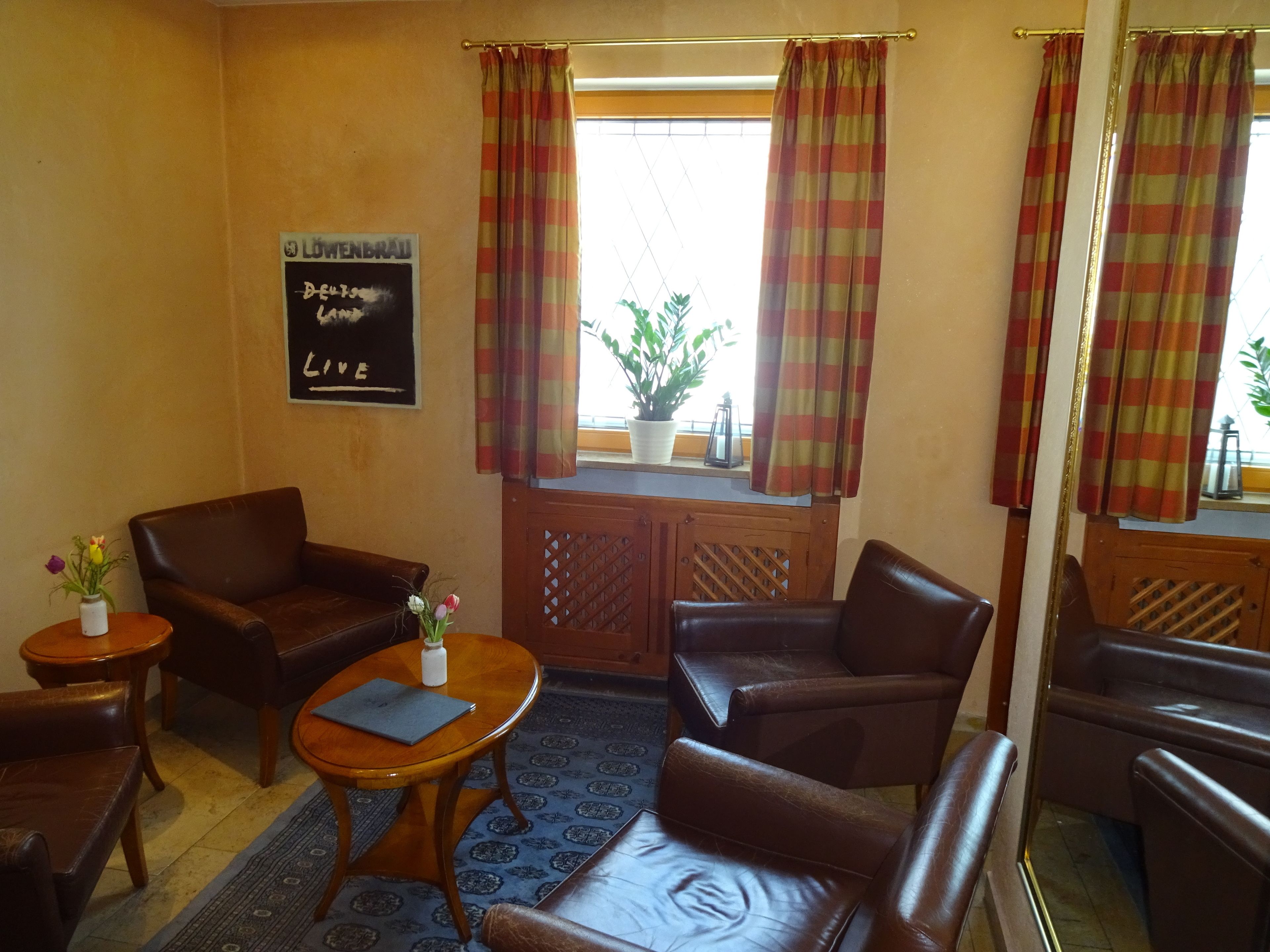 A cozy room with brown leather sofas, a wooden table with a laptop, and a potted plant by the window.