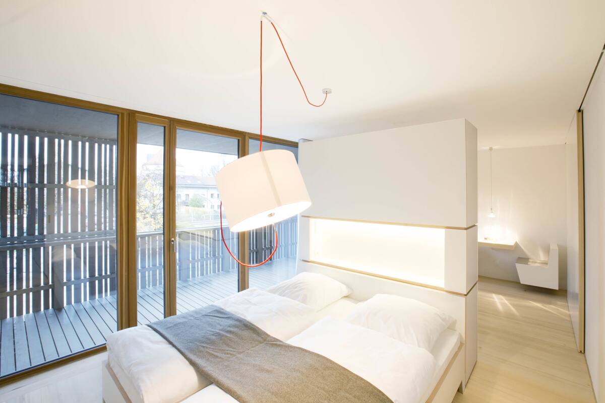 Une chambre moderne avec un grand lit, un luminaire suspendu et une vue dégagée grâce à de grandes fenêtres du sol au plafond.