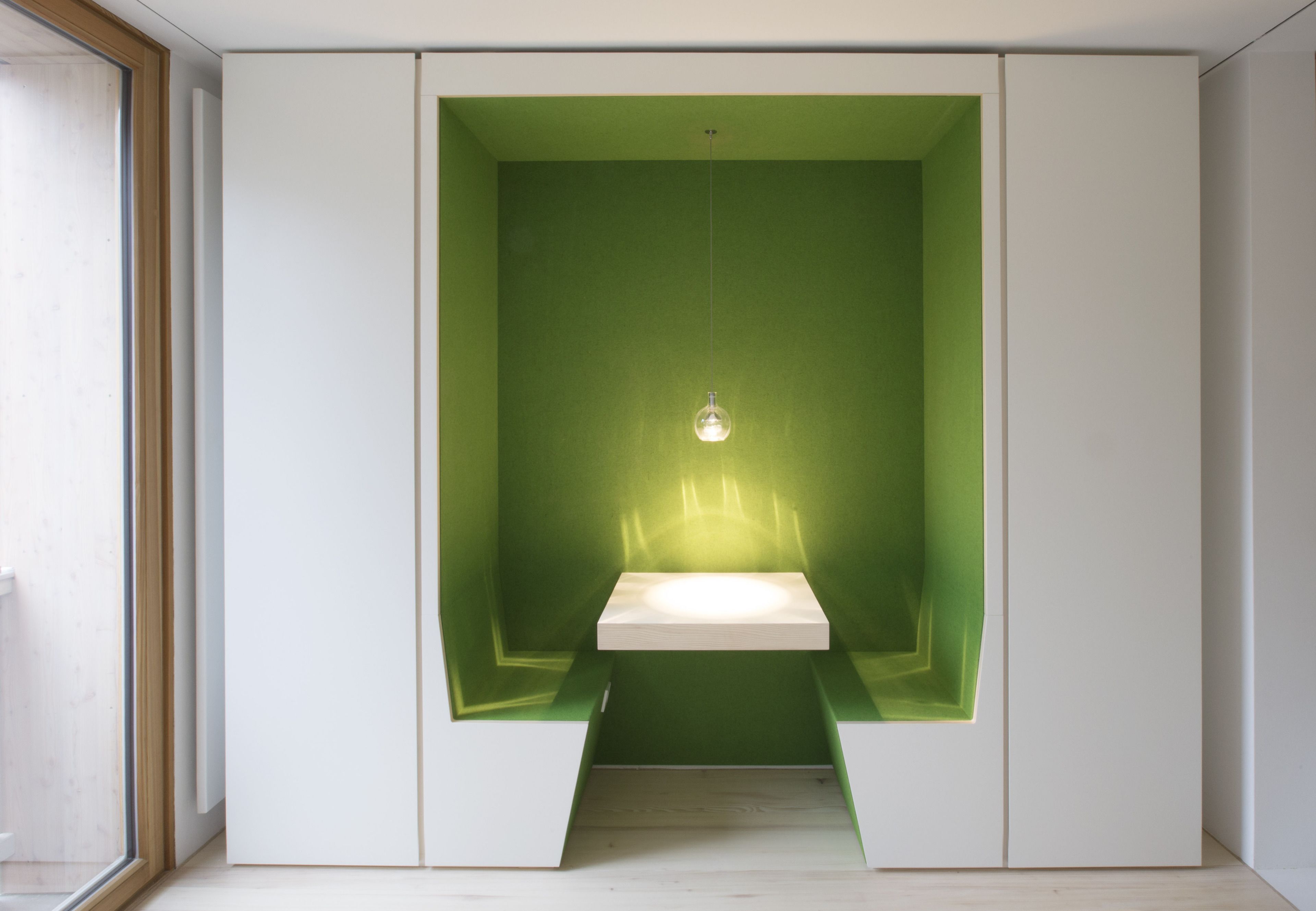 Een kamer met een groene accentmuur, een witte inbouwbank en een hanglamp.