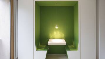 Een kamer met een groene accentmuur, een witte inbouwbank en een hanglamp.