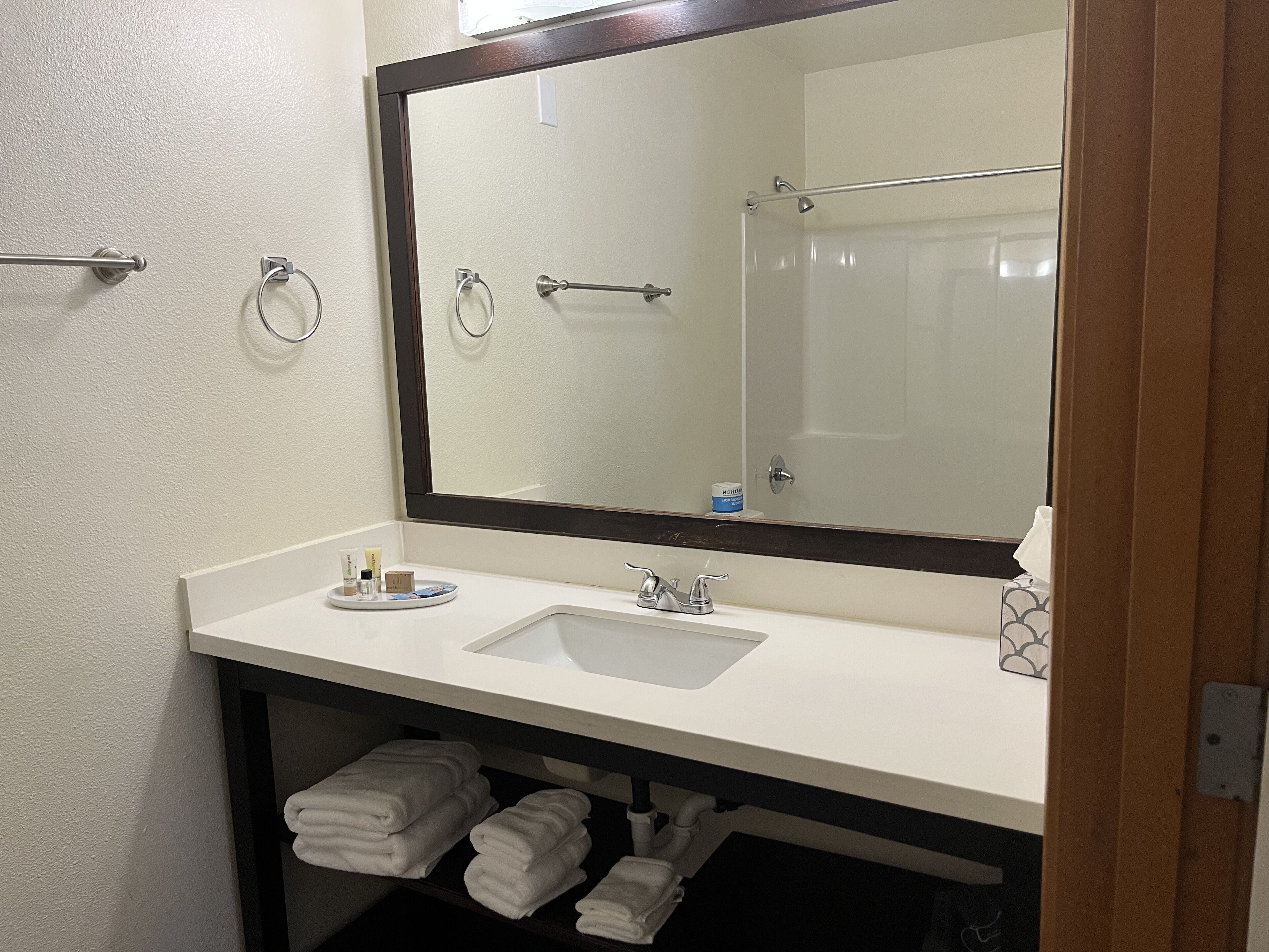 Un baño con lavamanos blanco, un espejo grande y un perchero para toallas.