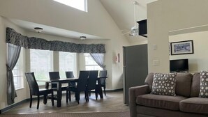 A spacious living room with a high ceiling, a dining area with a table and chairs, a sofa with patterned cushions, and a television on the wall. - Sunrise Inn Villas and Suites (Anacortes)