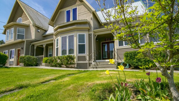 A two-story house with a bay window, a front porch, and a well-maintained lawn with flowers. - Sunrise Inn Villas and Suites (Anacortes)