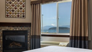 A hotel room with a fireplace, a view of the sea, and a decorative wall piece. - Sunrise Inn Villas and Suites (Anacortes)