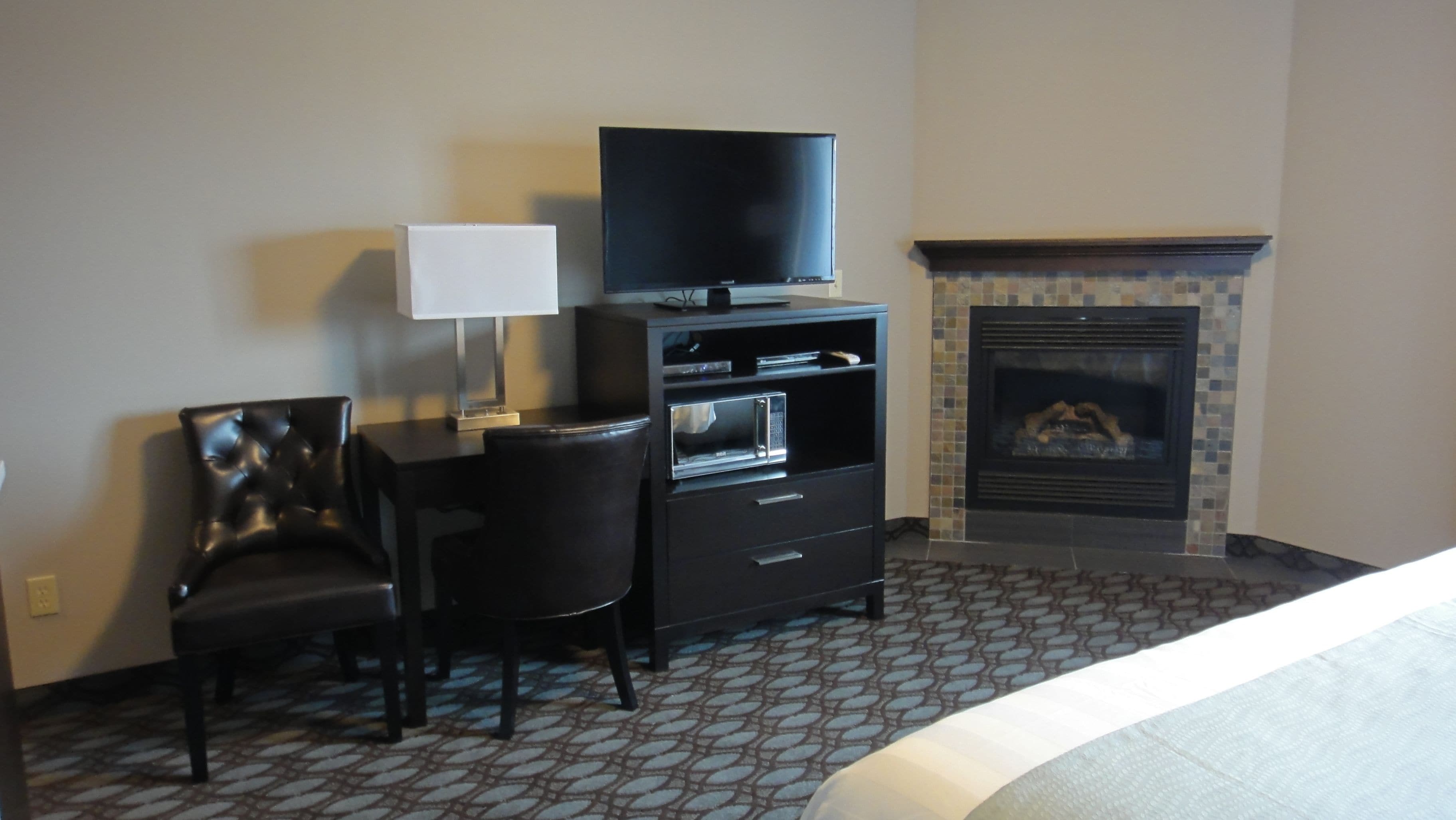 Habitación de hotel con cama, escritorio con silla, televisor sobre un mueble, microondas y chimenea.