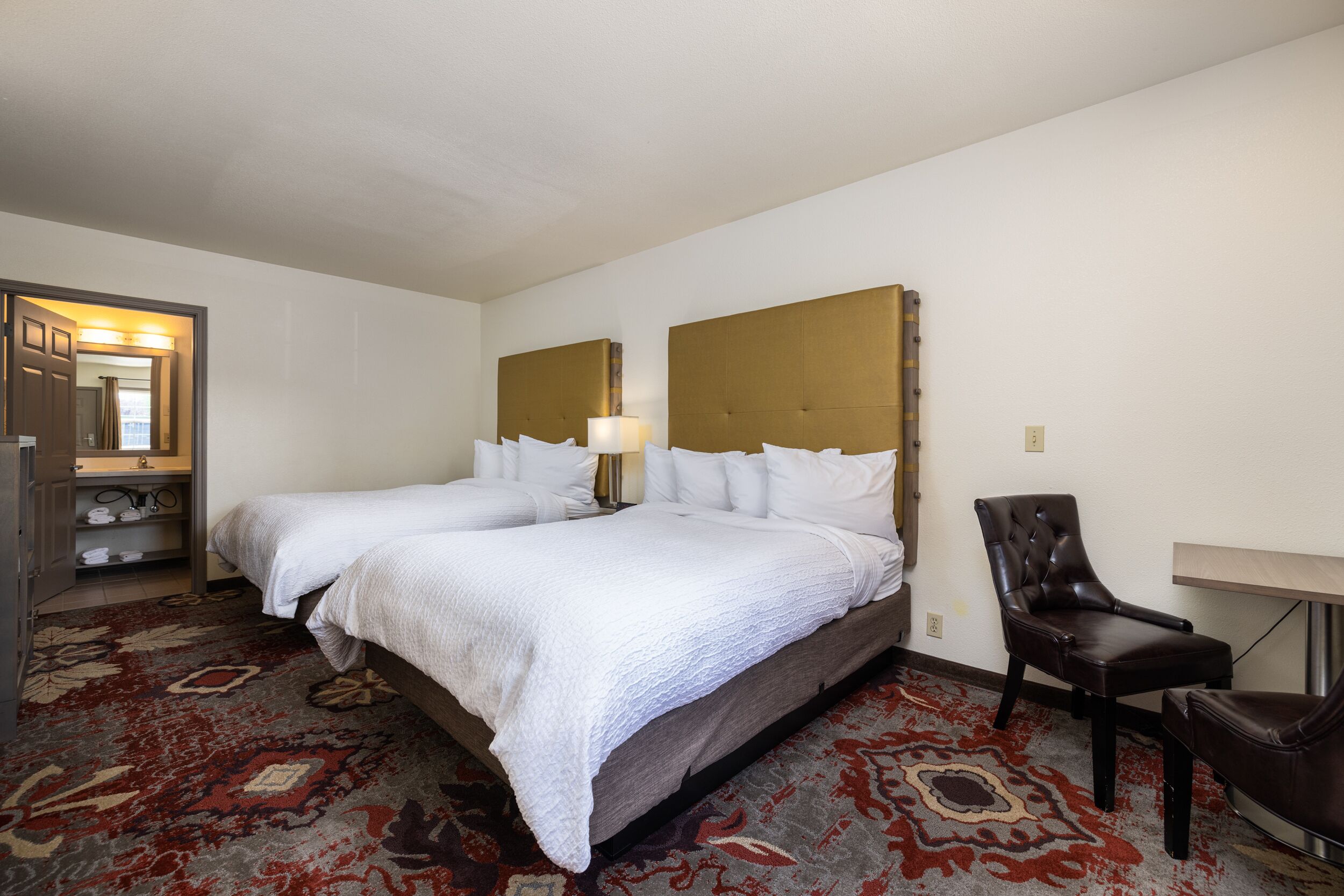 Habitación de hotel con dos camas, una silla, un escritorio y suelo alfombrado.